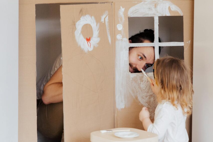 a little girl and her dad painting a cardboard house